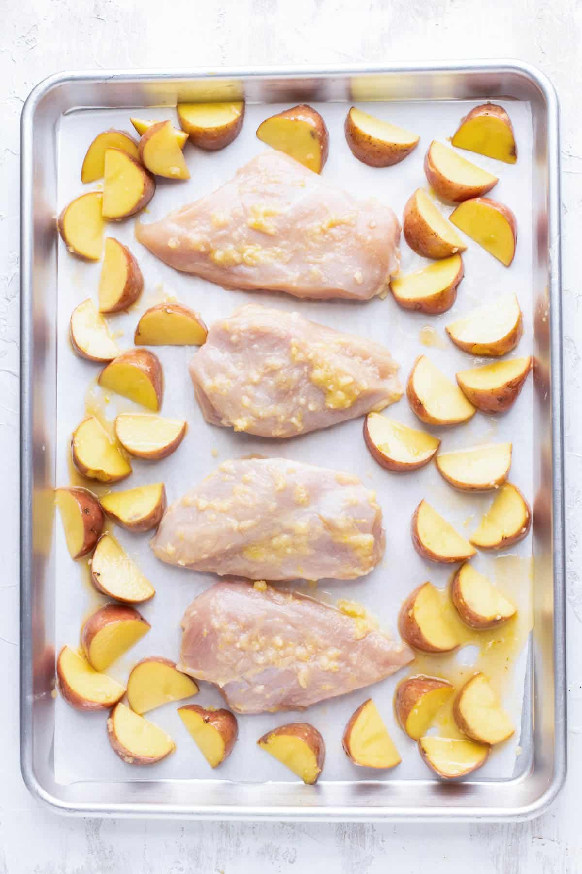 Chicken and potatoes are spread on a baking sheet.