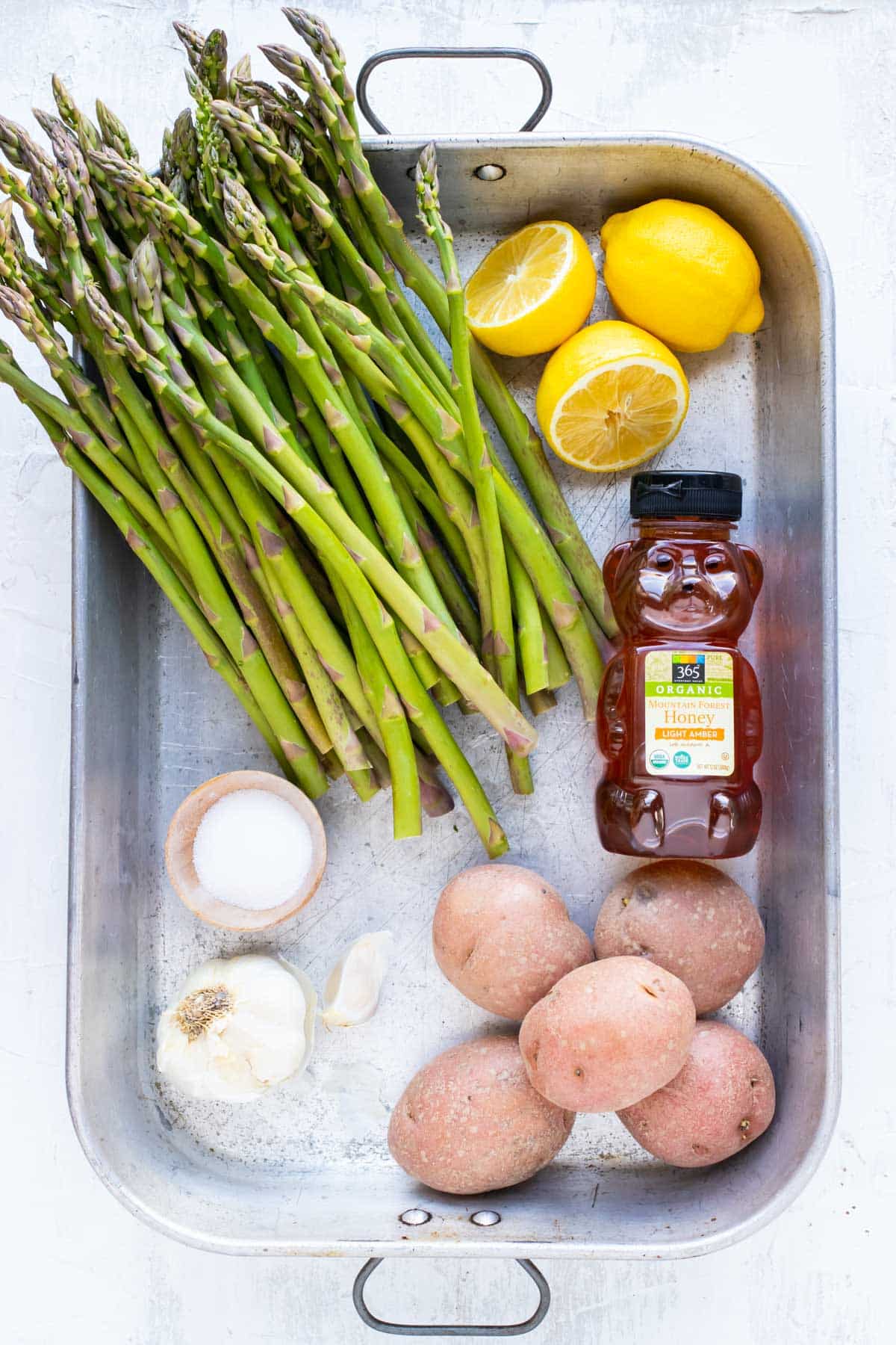 Asparagus, fresh lemons, honey, red potatoes, garlic, and salt as the ingredients in a baked lemon garlic chicken recipe.