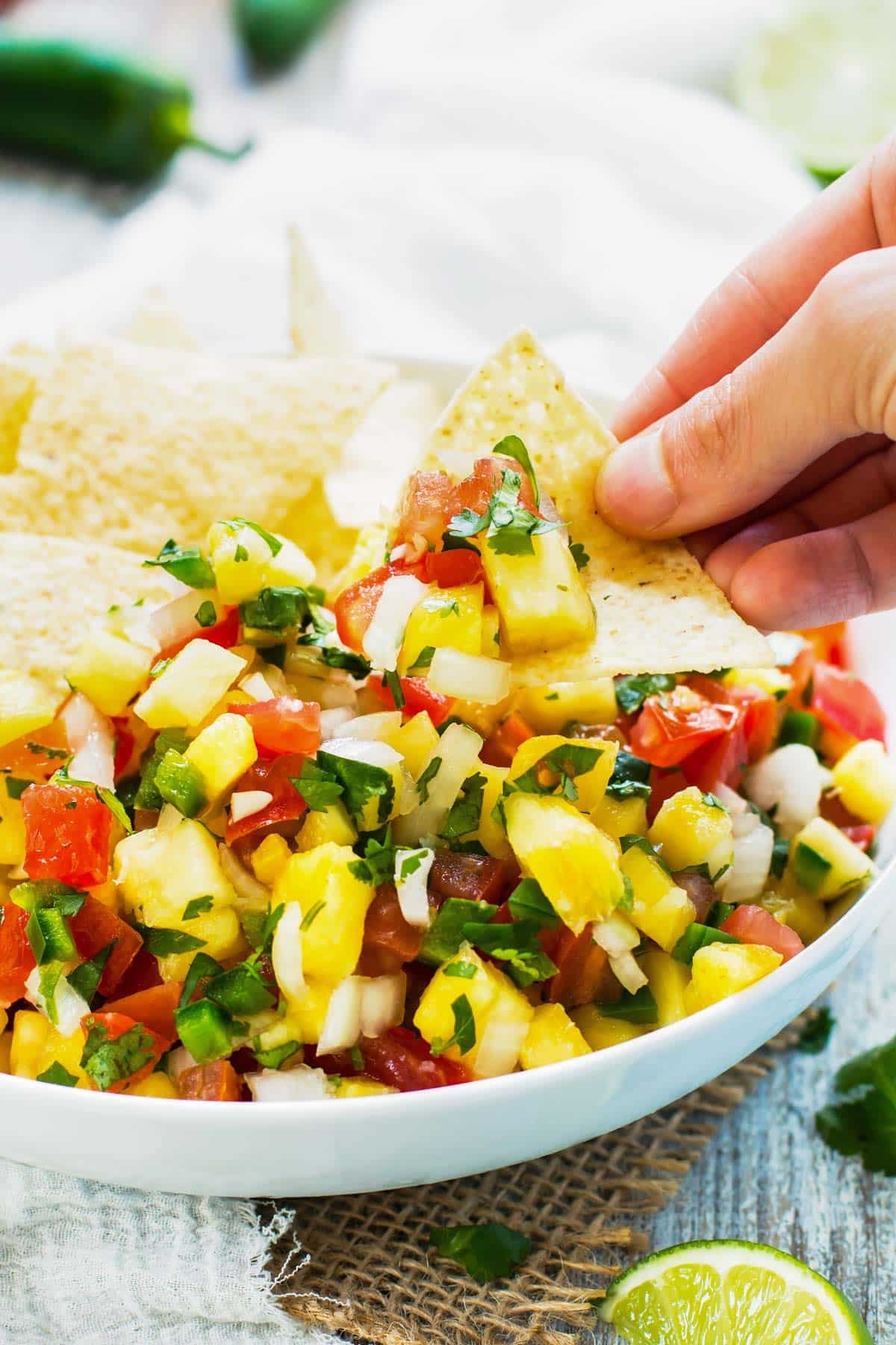 A hand using a tortilla chip to scoop a serving of a Pineapple Pico de Gallo recipe for lunch.