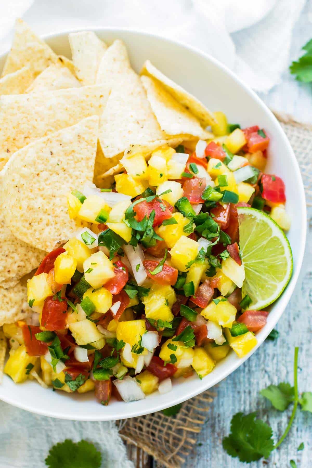 Pineapple Pico de Gallo RECIPE served in a white bowl, a lime, and tortilla chips.