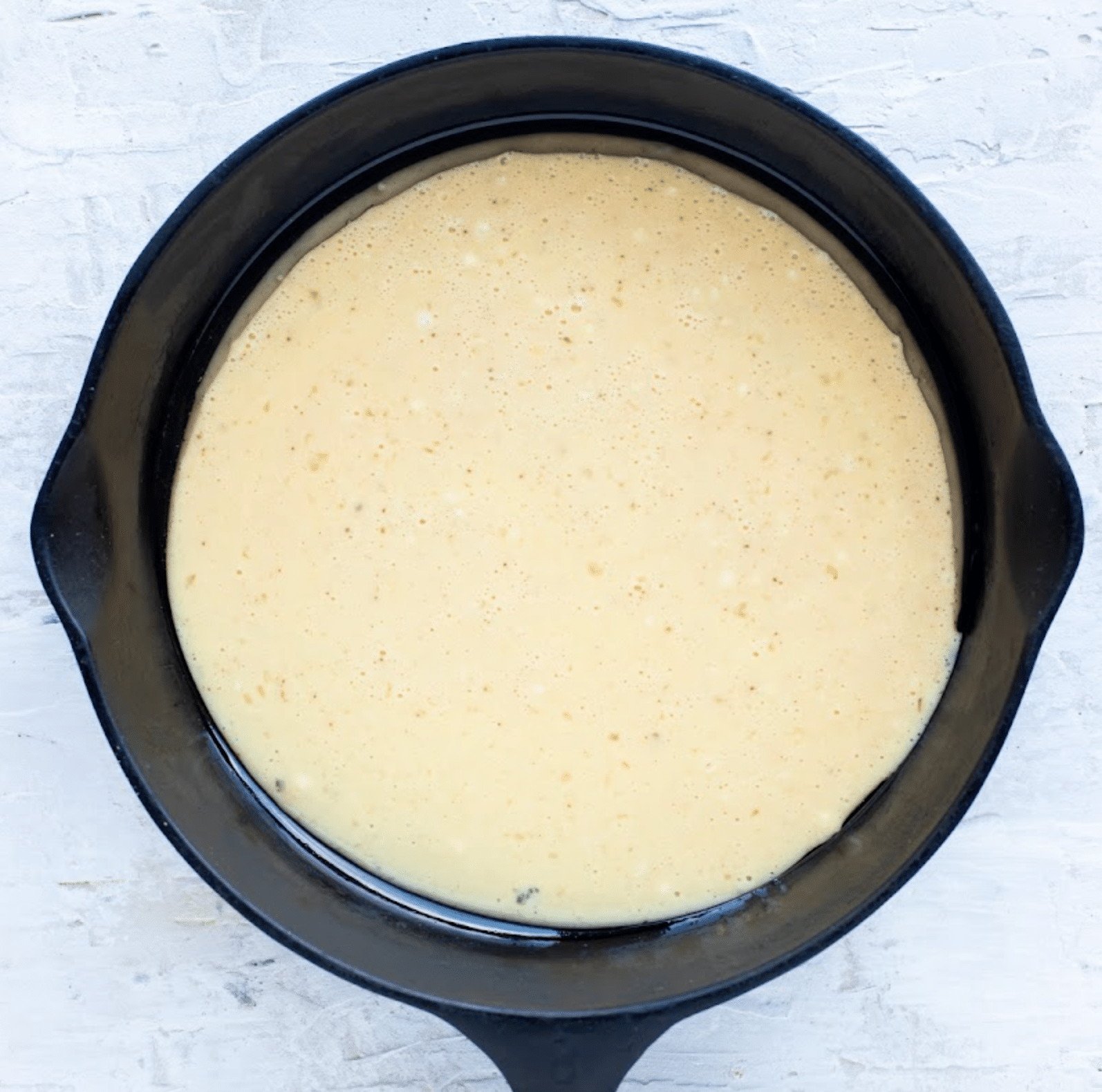 The pancake batter is poured into the hot cast iron skillet.