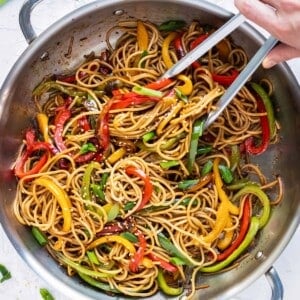 Sesame noodles are tossed in a wok with bell peppers and served with green onions for a quick dinner.