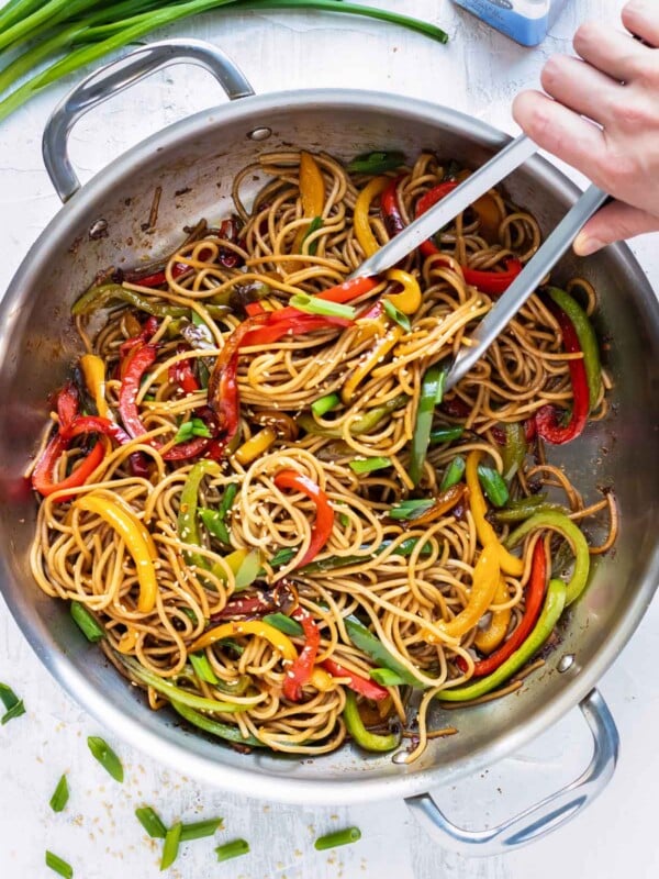 Sesame noodles are tossed in a wok with bell peppers and served with green onions for a quick dinner.