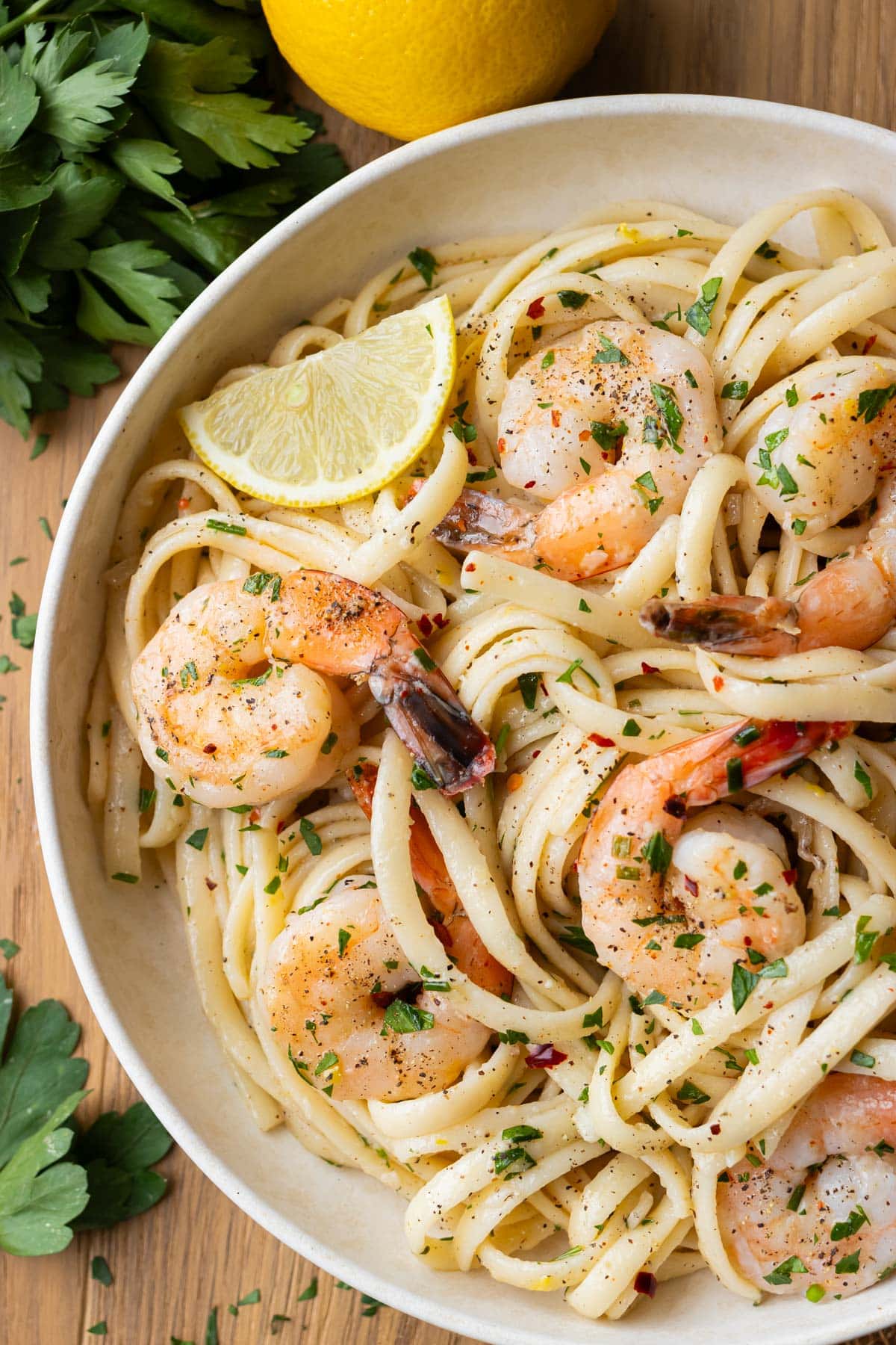 A bowl full of shrimp scampi linguine is served with a lemon wedge and fresh parsley on top.