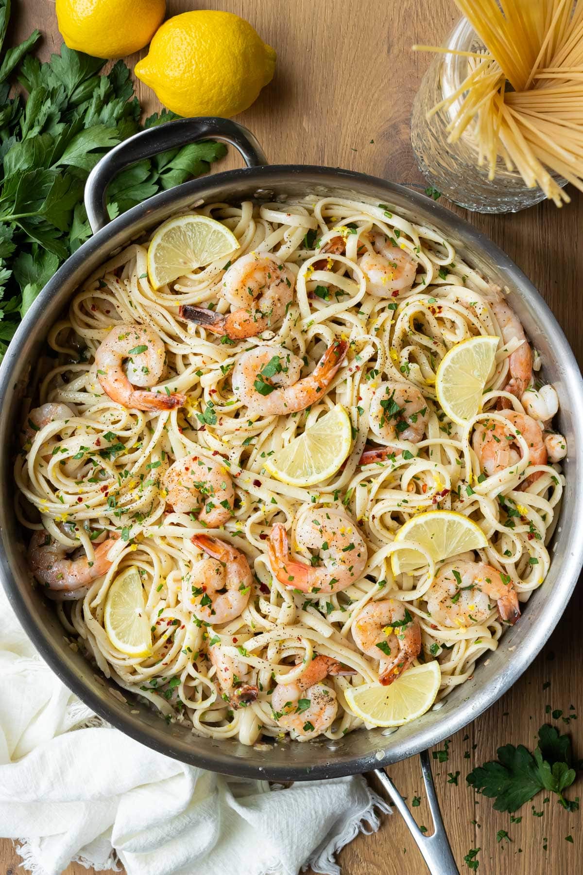 A stainless steel skillet is full of shrimp scampi with linguine pasta and a lemon butter garlic sauce.