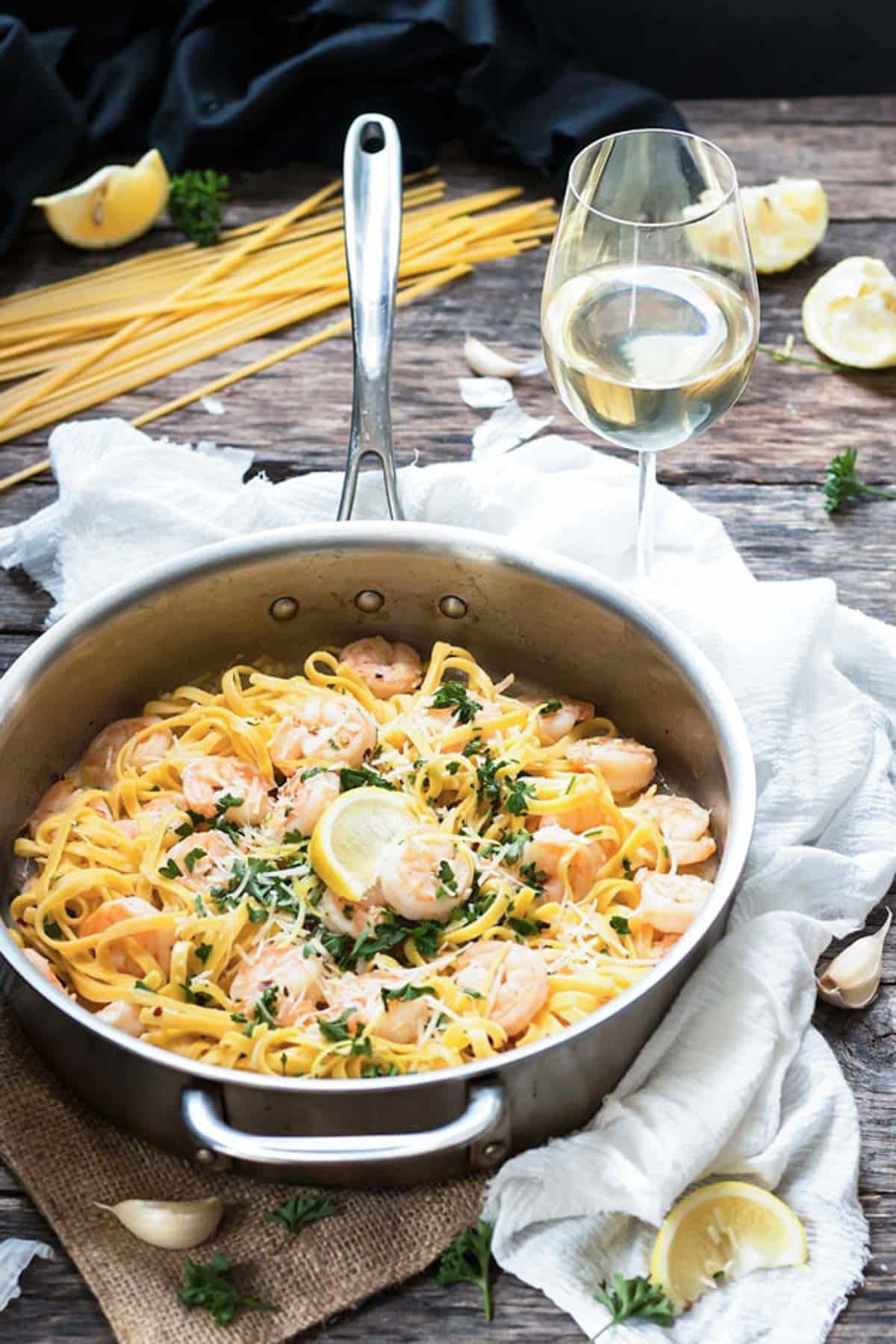 A silver pan filled with Easy Shrimp Scampi Linguine with a glass of white wine for a light dinner.