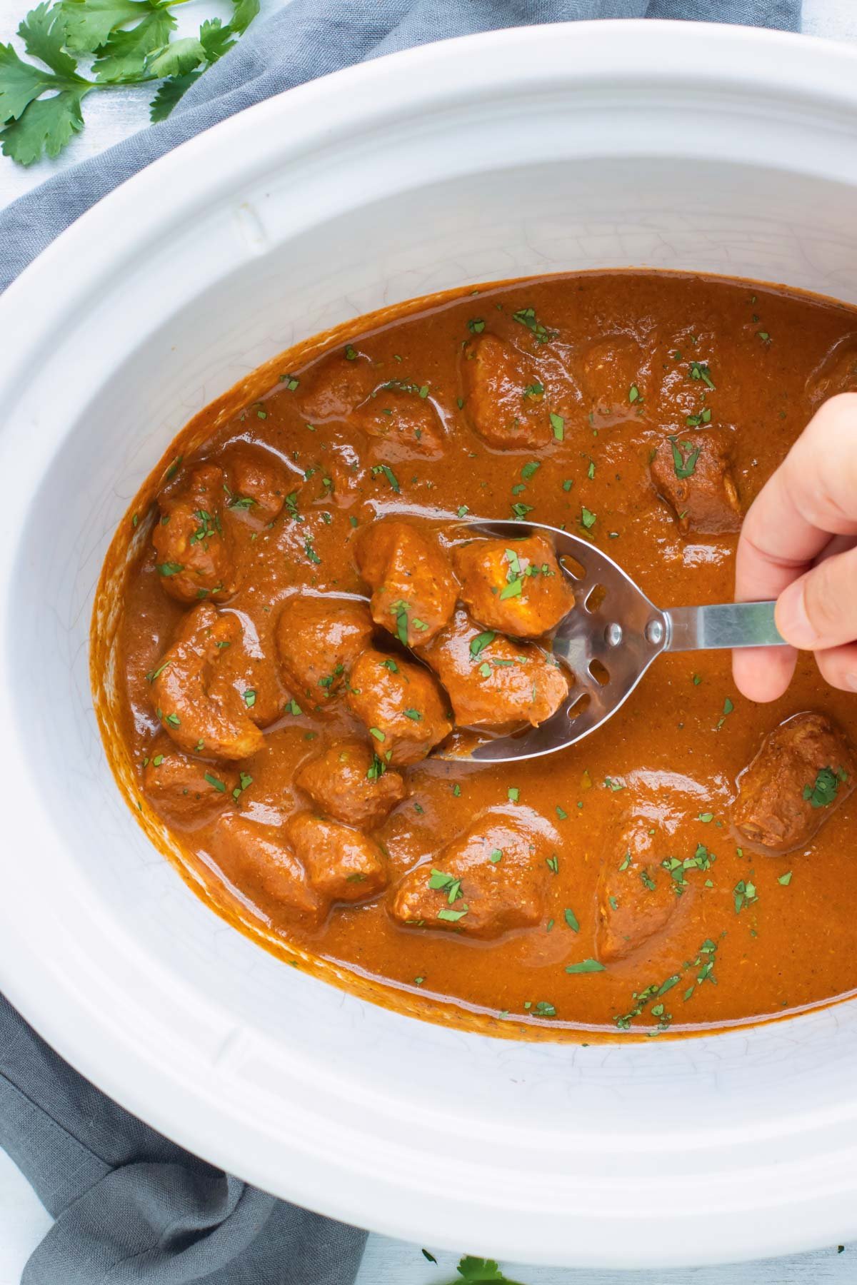 Easy Chicken Tikka Masala in a slow cooker scooped up by a silver spoon.
