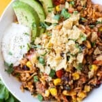 A Mexican beef and rice skillet recipe is served in a white bowl with tortilla chips and sour cream.