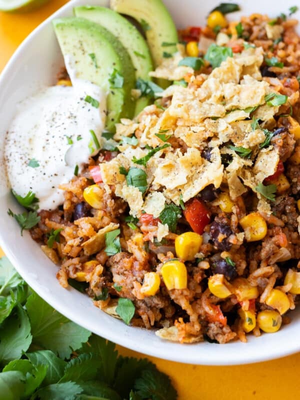 A Mexican beef and rice skillet recipe is served in a white bowl with tortilla chips and sour cream.