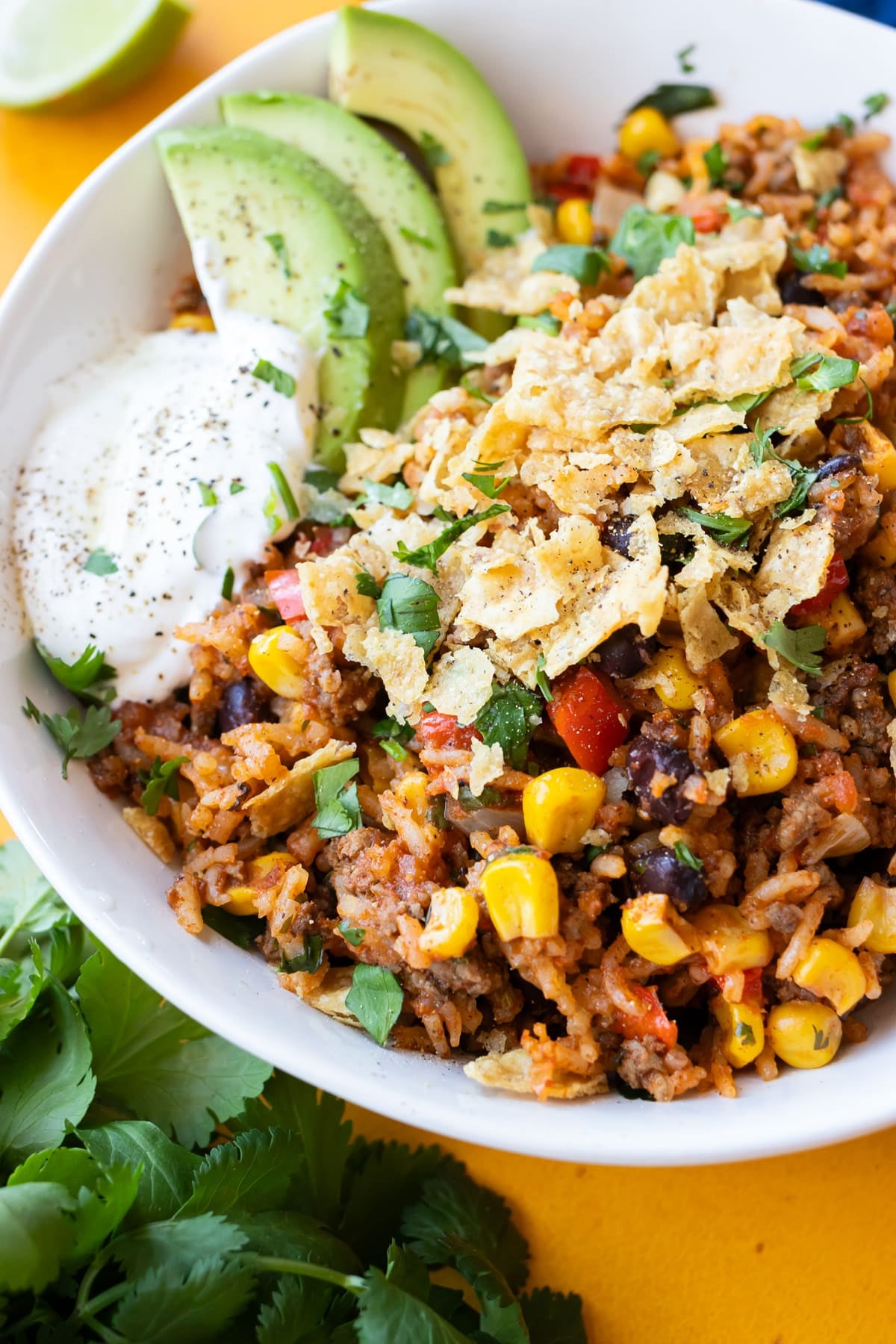A Mexican beef and rice skillet recipe is served in a white bowl with tortilla chips and sour cream.