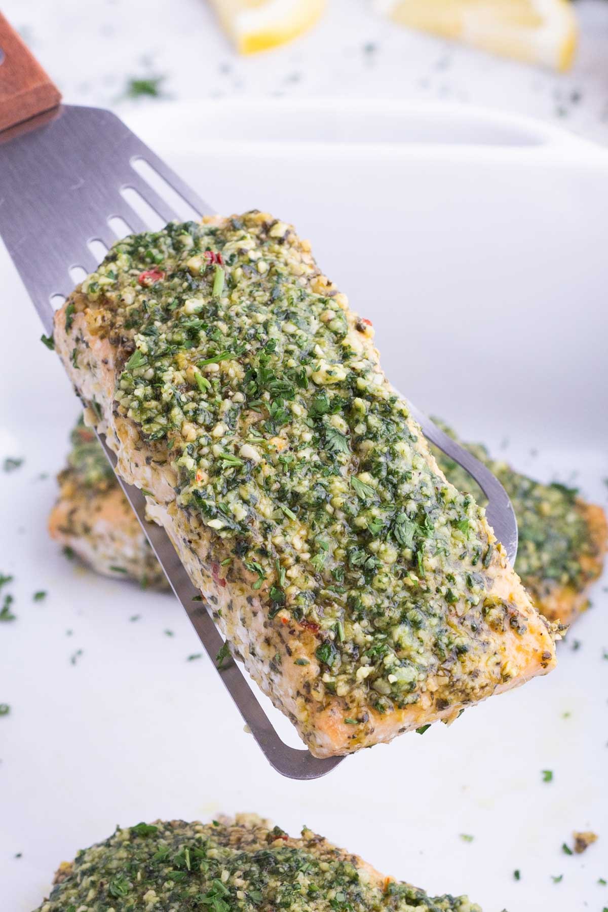 A spatula lifts a pesto salmon filet out of the baking dish.