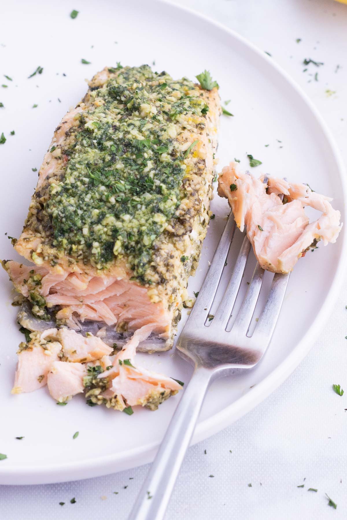 A fork digs into a pesto salmon filet.