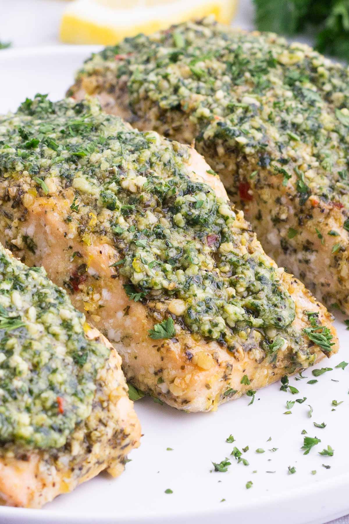 Salmon filets with pesto are served on a white plate.