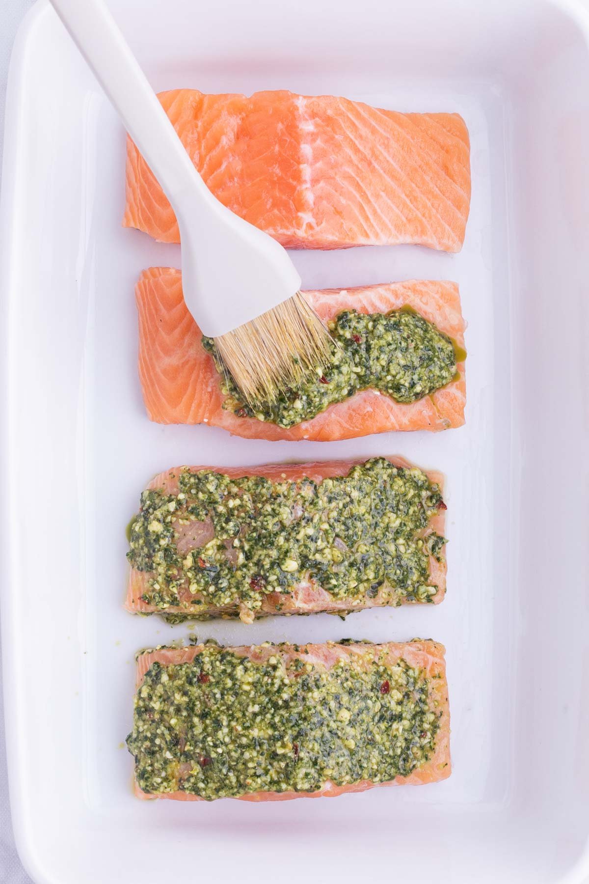 Pesto sauce is brushed over salmon filets.