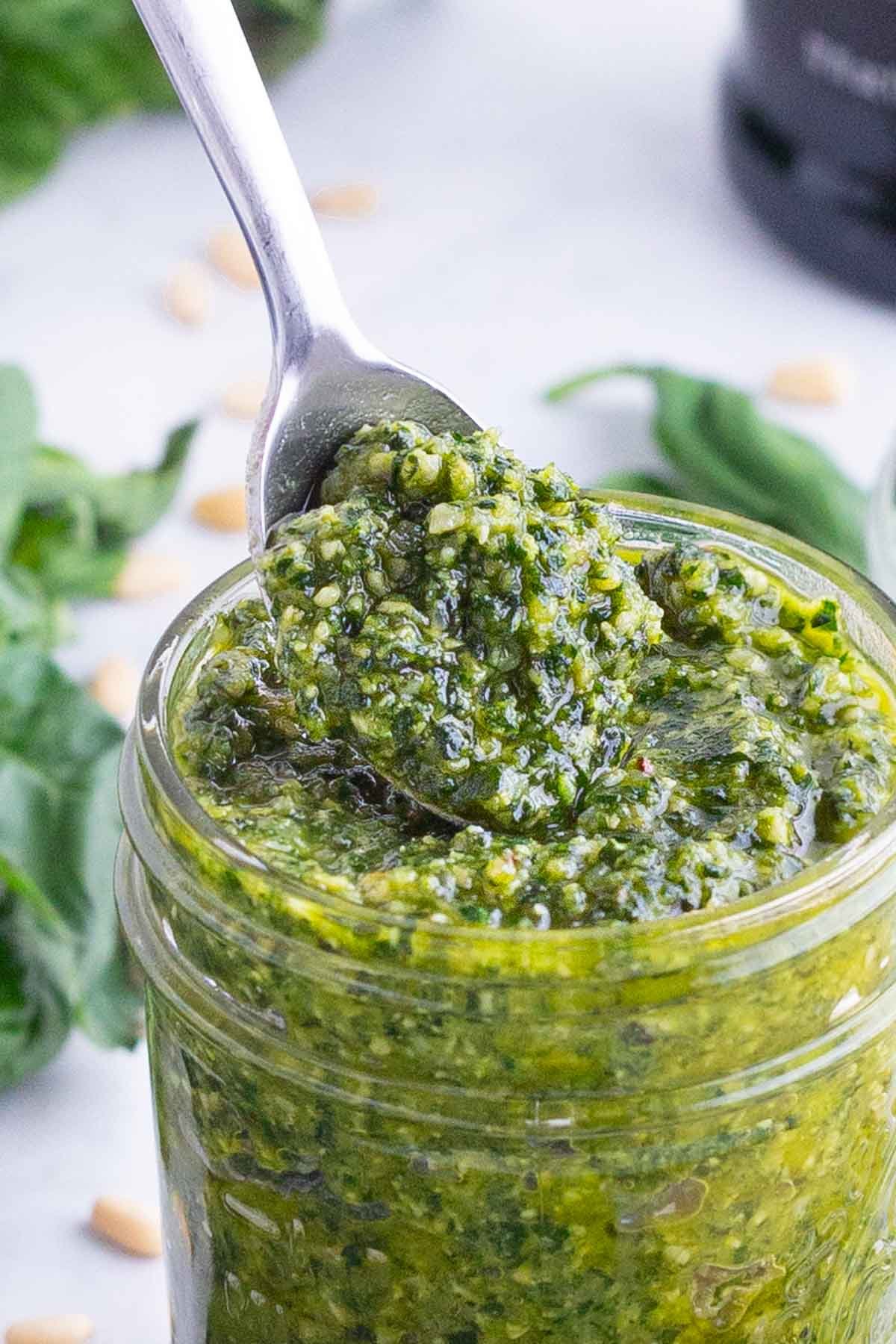 A metal spoon is lifting some healthy, fresh basil sauce.