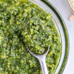 A metal spoon is lifting some healthy, fresh basil sauce.