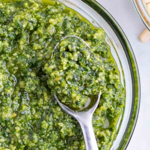 A metal spoon is lifting some healthy, fresh basil sauce.