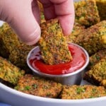 A hand dips a homemade broccoli tot into a bowl of ketchup.