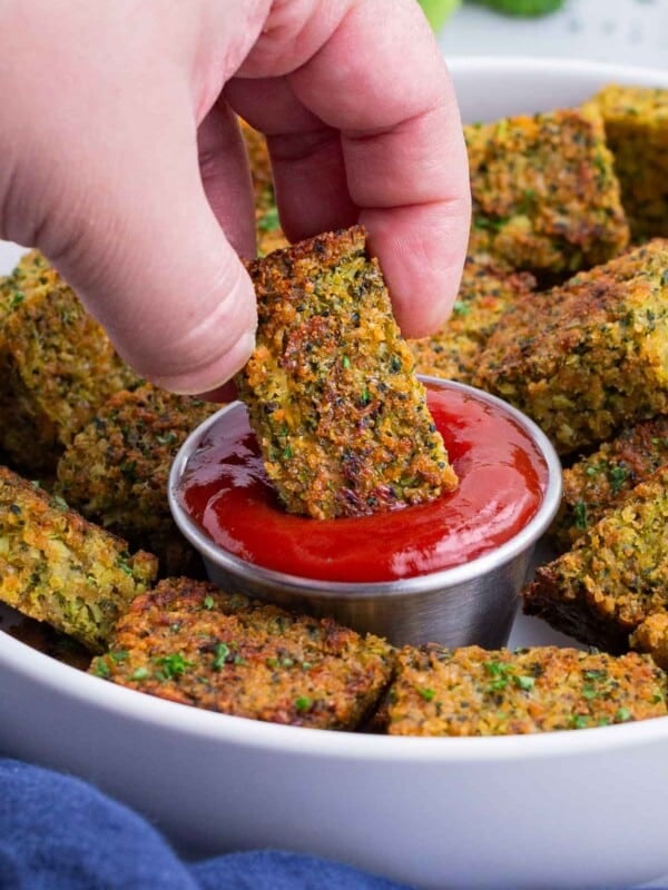 A hand dips a homemade broccoli tot into a bowl of ketchup.