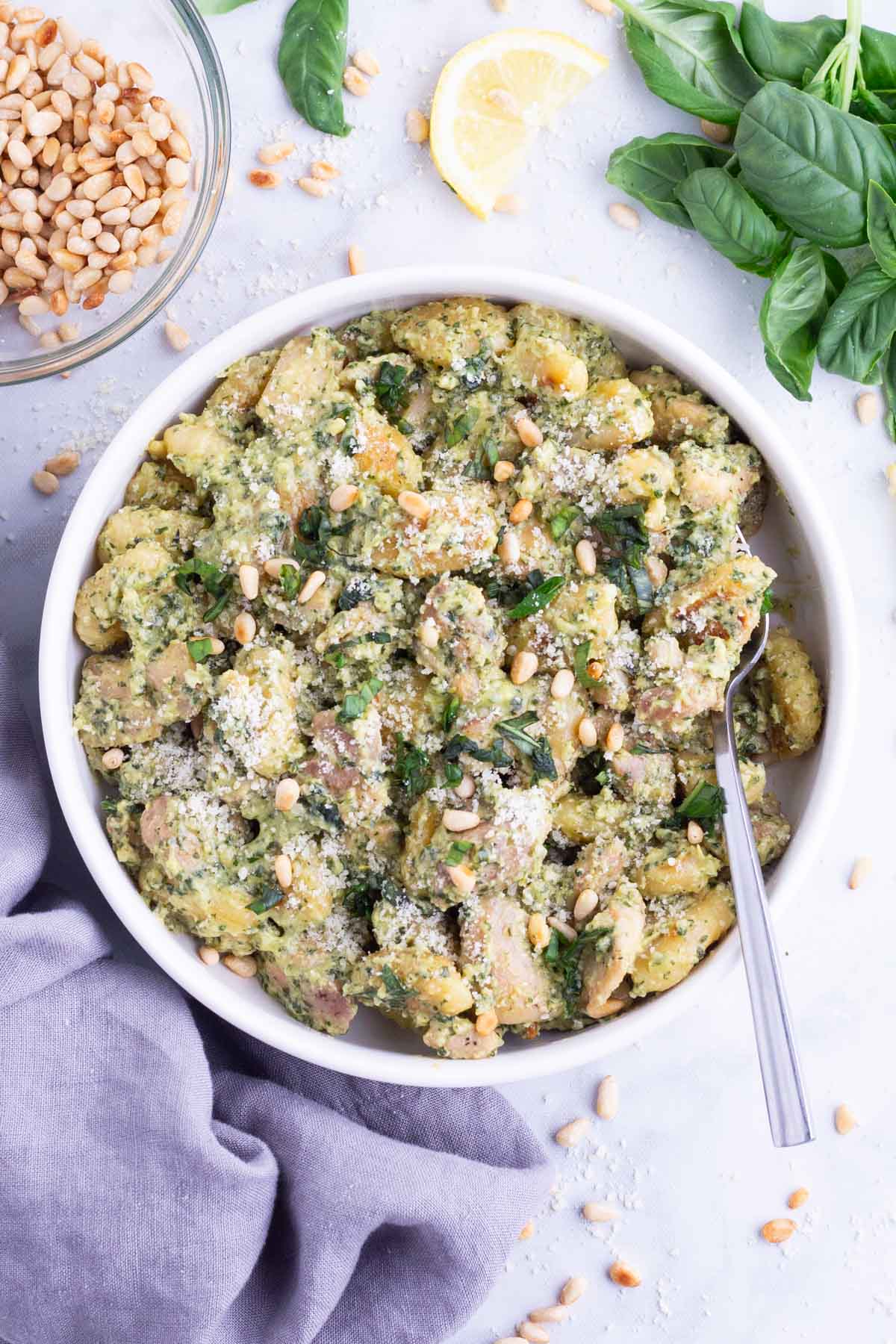 A white bowl is full of chicken and gnocchi in a creamy pesto sauce.