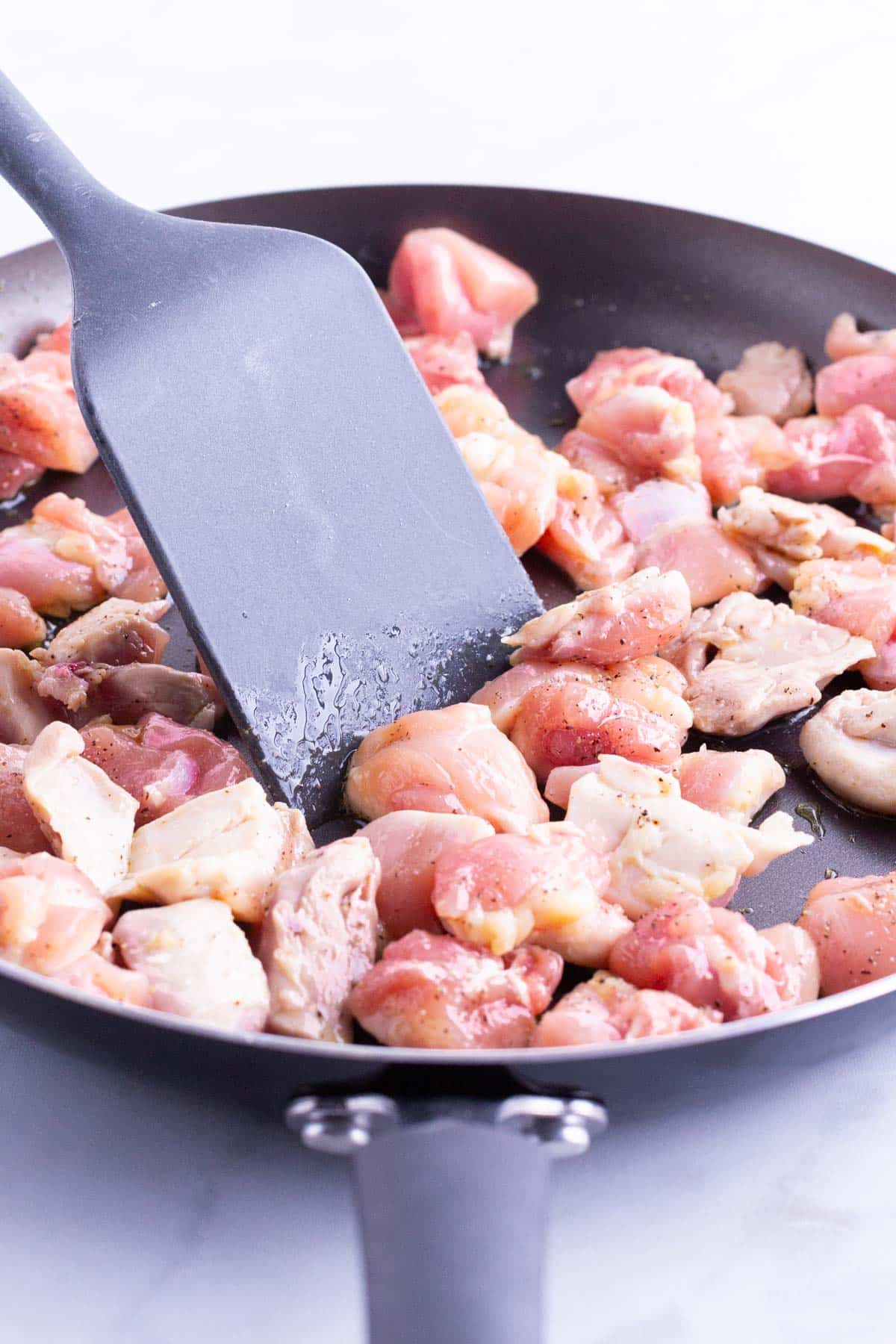 Chicken thighs are sauteed in a skillet.