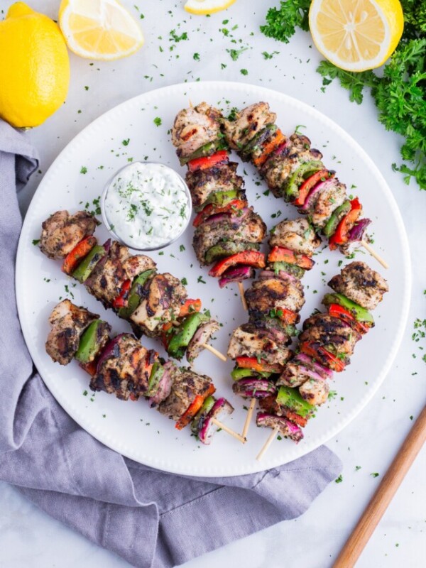 Greek chicken kabobs are served on a white plate with Tzatziki sauce.