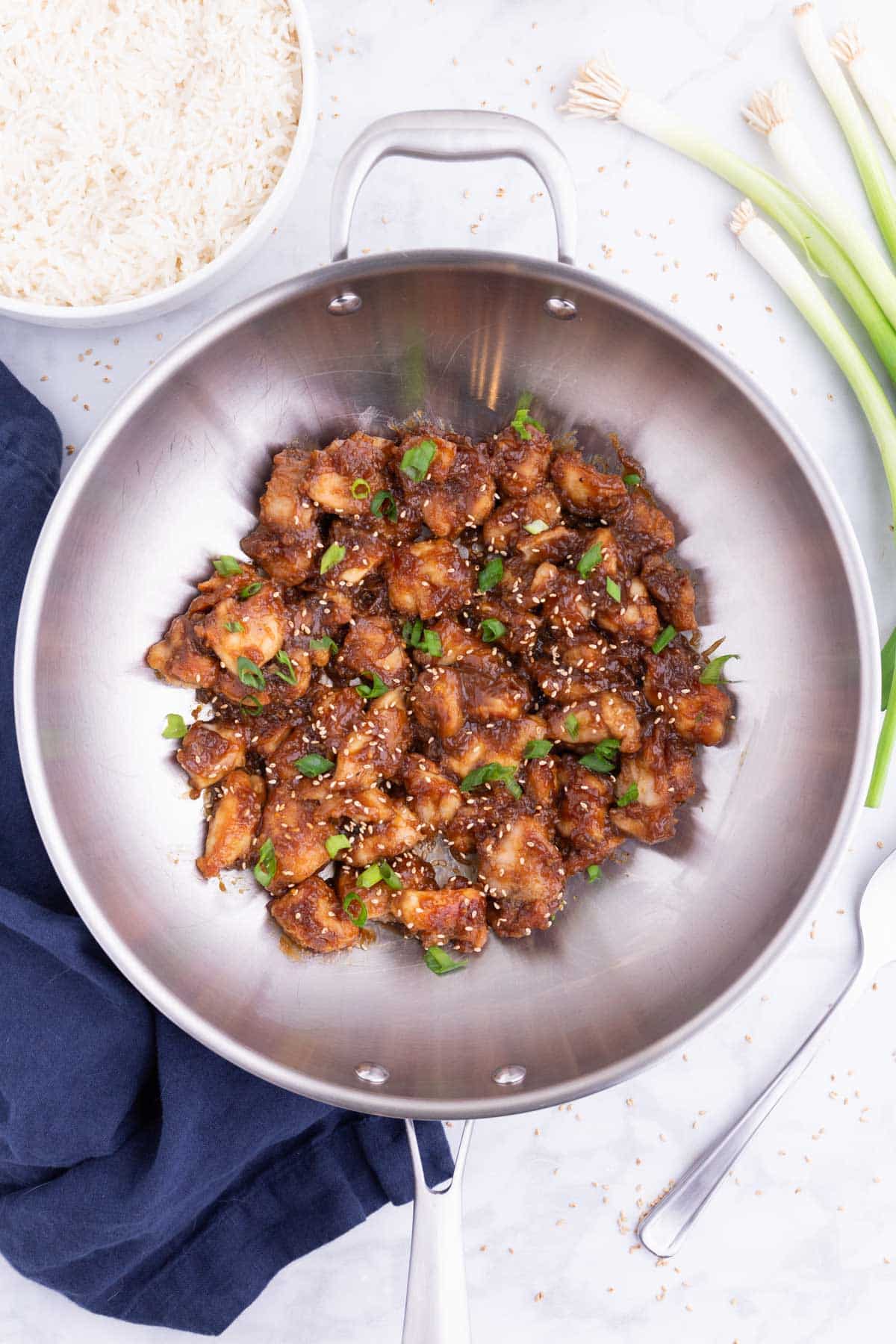 The orange sauce is mixed with cooked chicken in a wok.