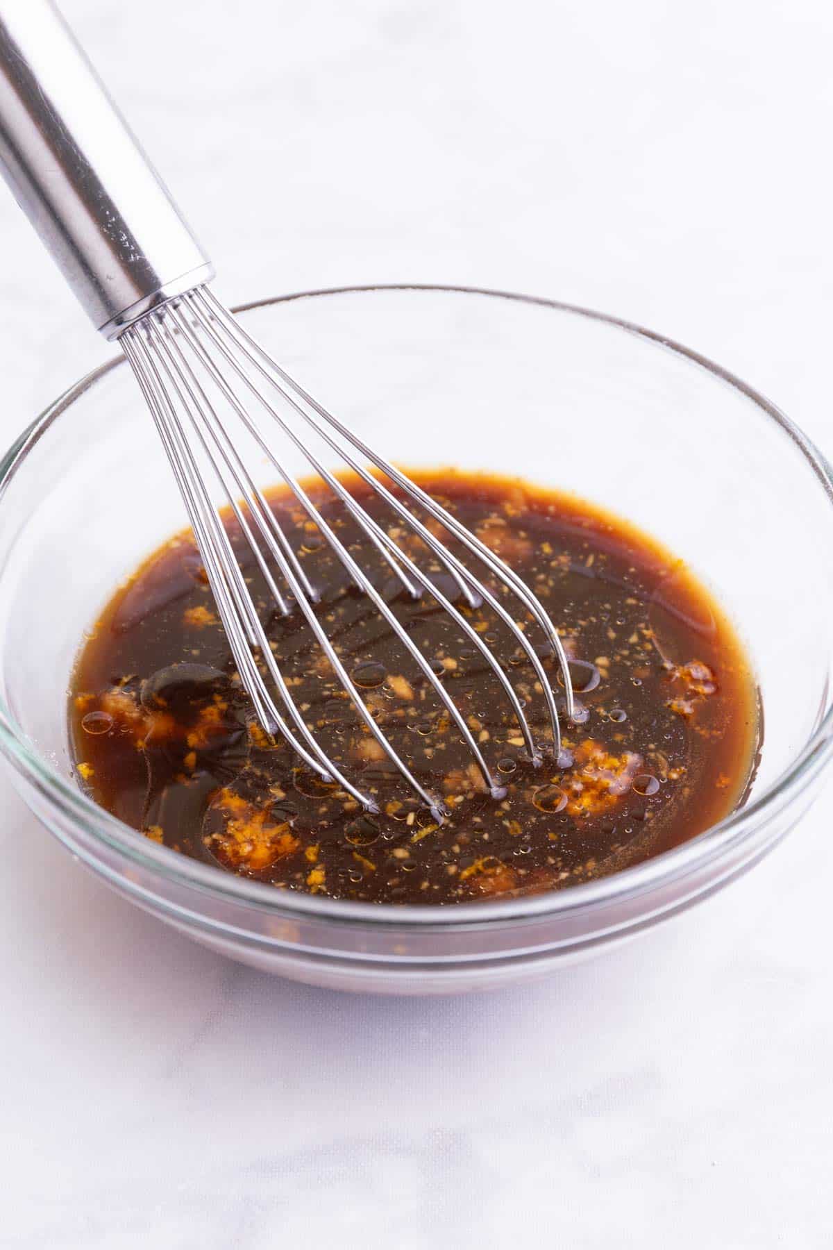An orange sauce is whisked together in a glass bowl.