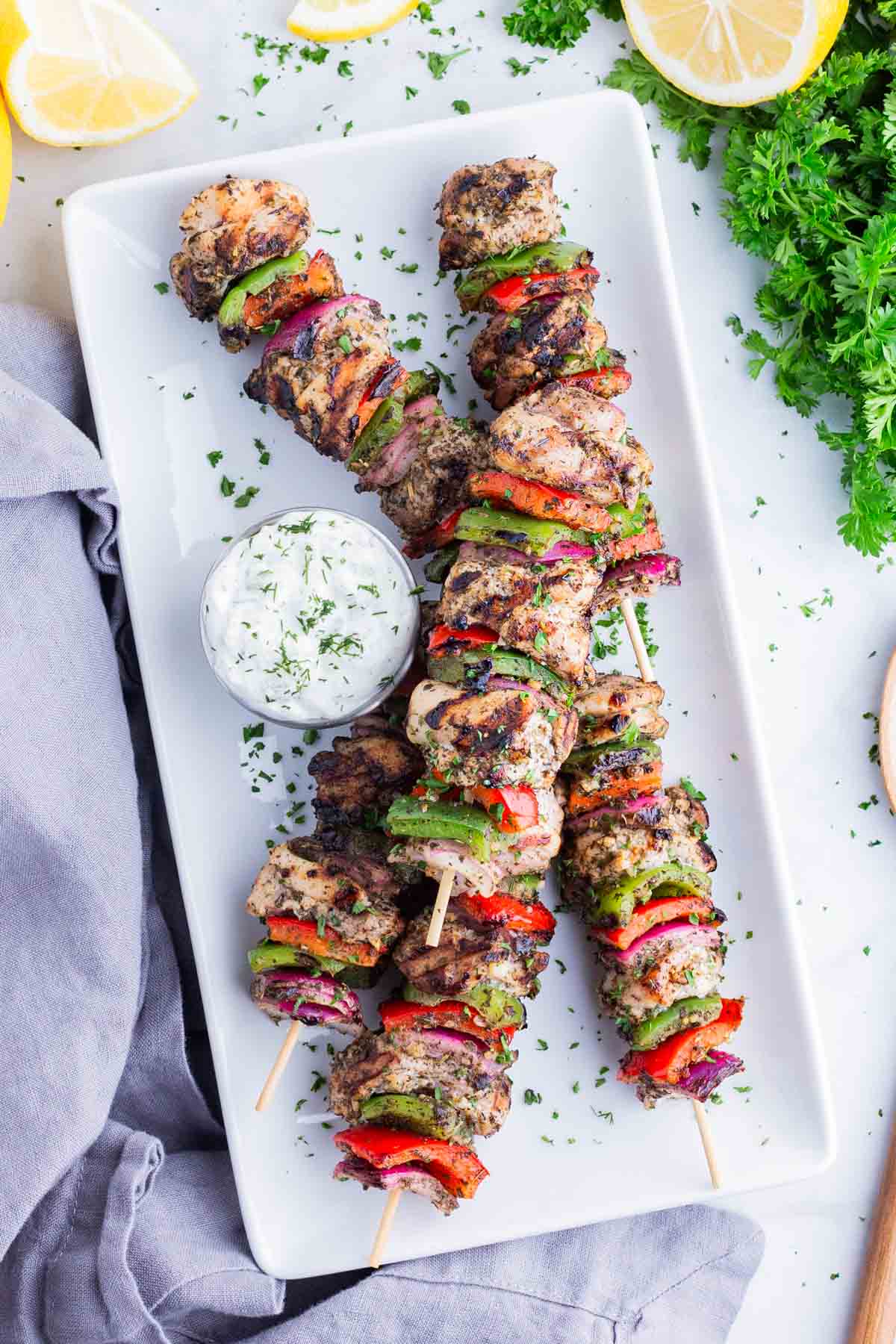 Greek chicken kabobs are served on a white plate with Tzatziki sauce.