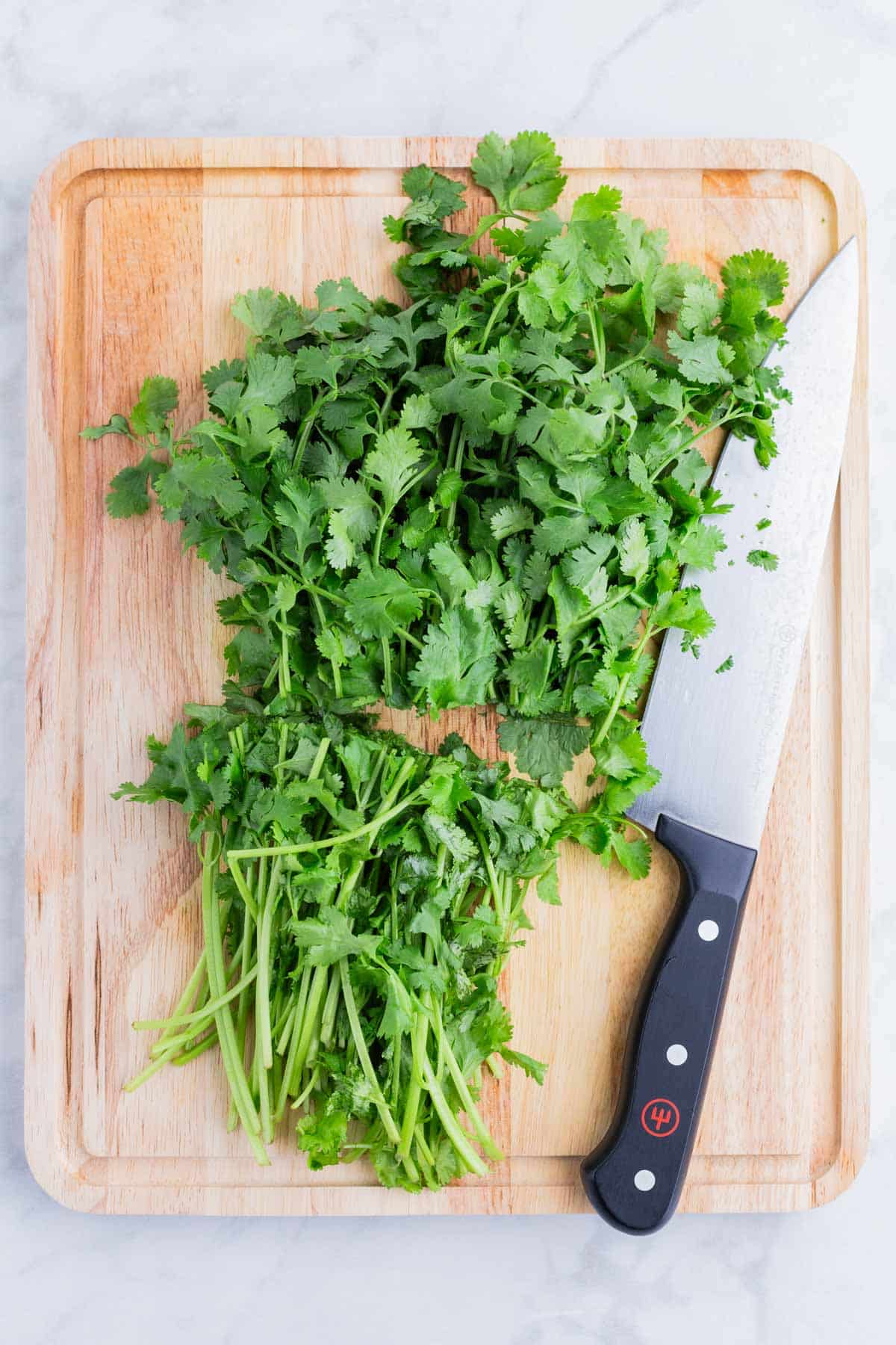 A sharp knife sits next to a pile of cilantro.