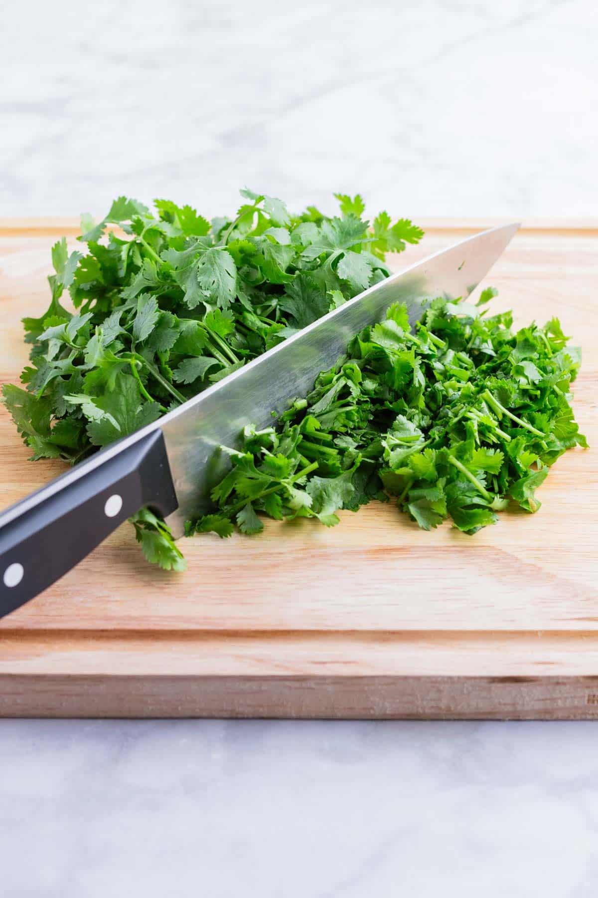 A pile of fresh cilantro is chopped on a cutting board.