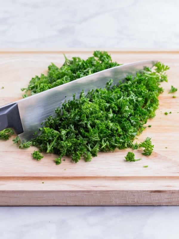 A sharp knife chops a pile of parsley.