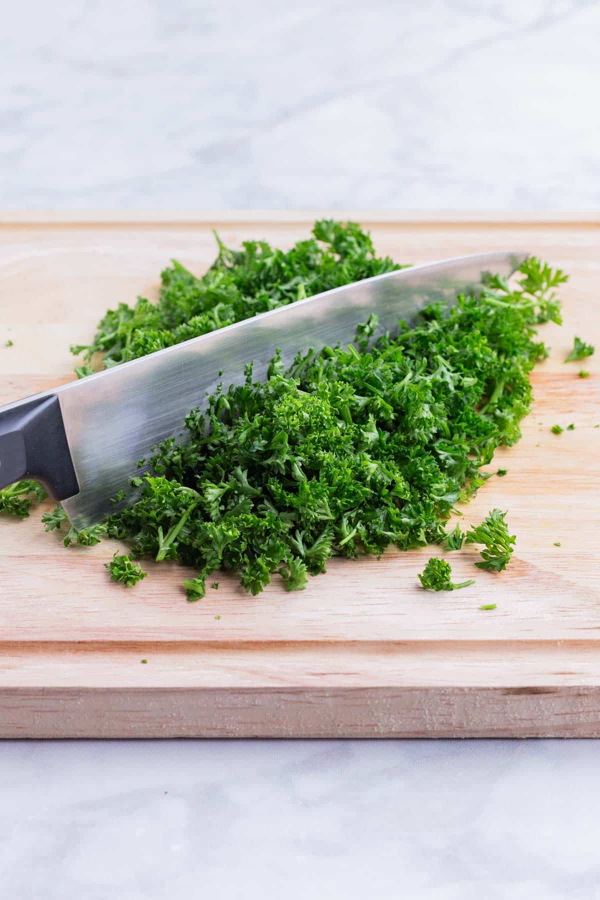 A sharp knife chops a pile of parsley.