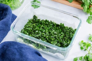 Chopped cilantro is stored in a glass container.