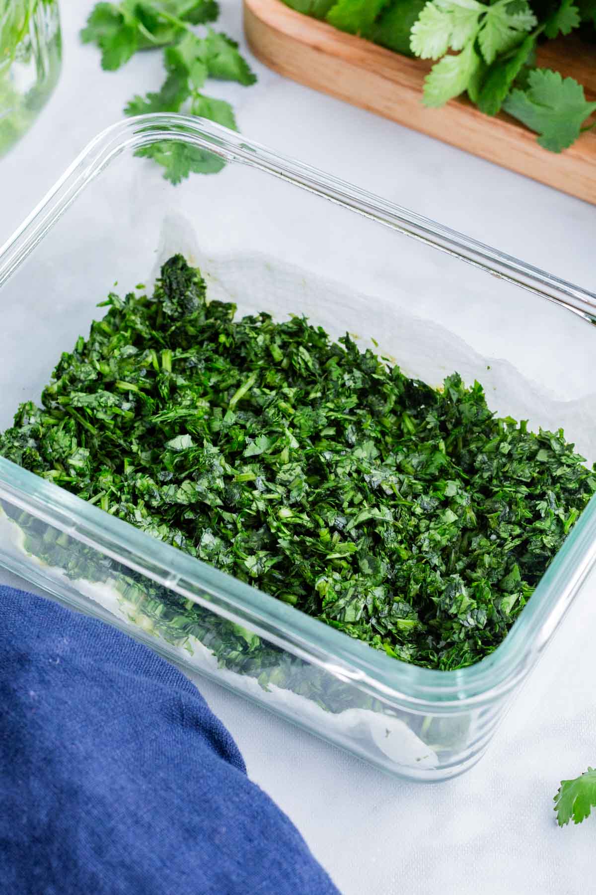 Chopped cilantro is stored in a glass container.