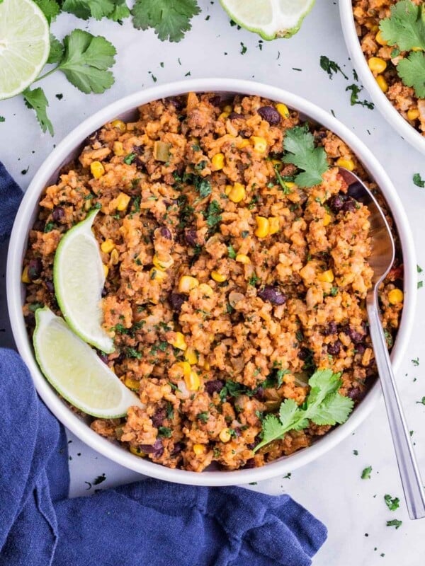 A one-pot Mexican Beef and Rice recipe is served in a white bowl for dinner with cilantro and lime wedges.