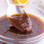 A spoon scoops out some orange sauce from a bowl.