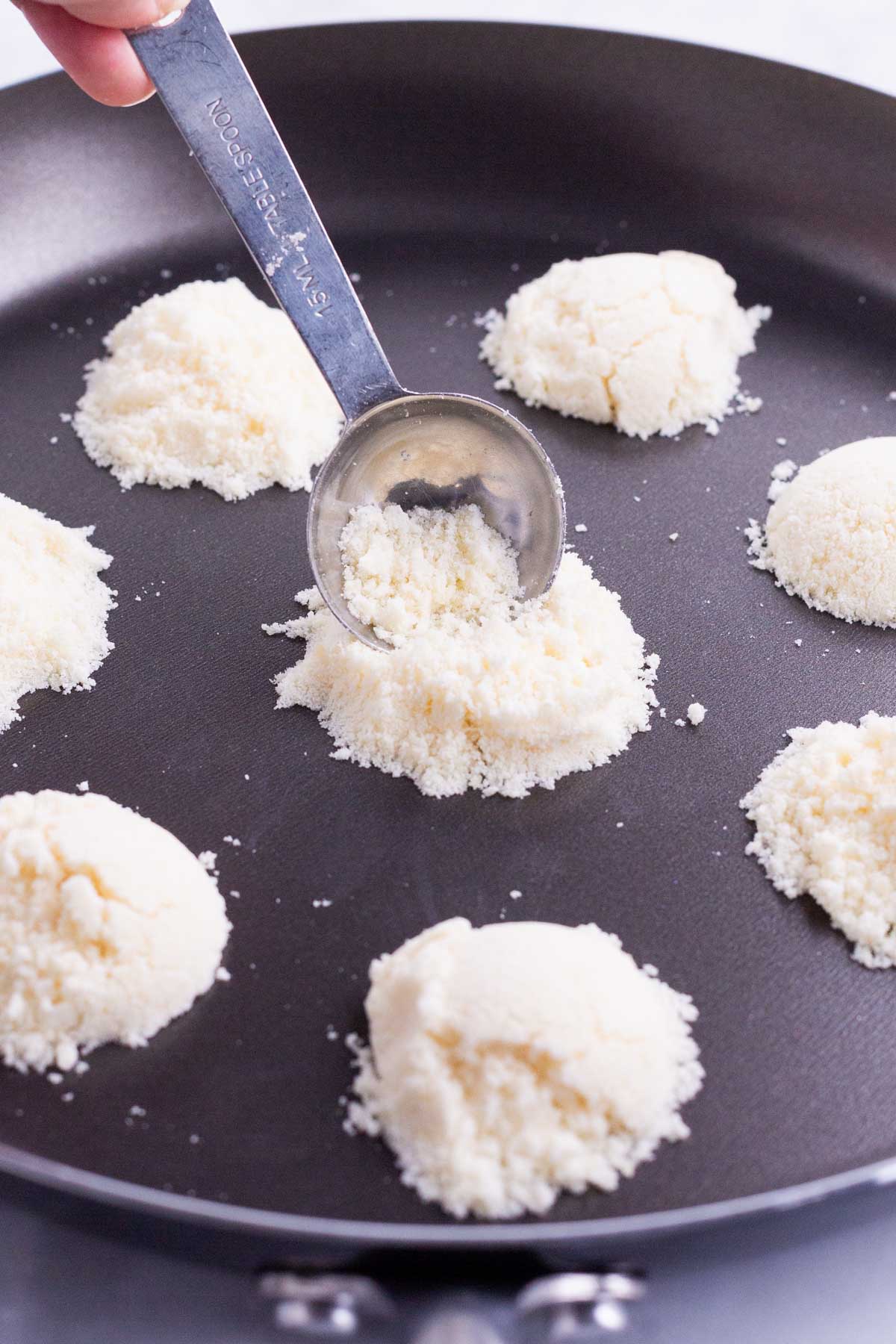 A spoon scoops Parmesan cheese onto a skillet.