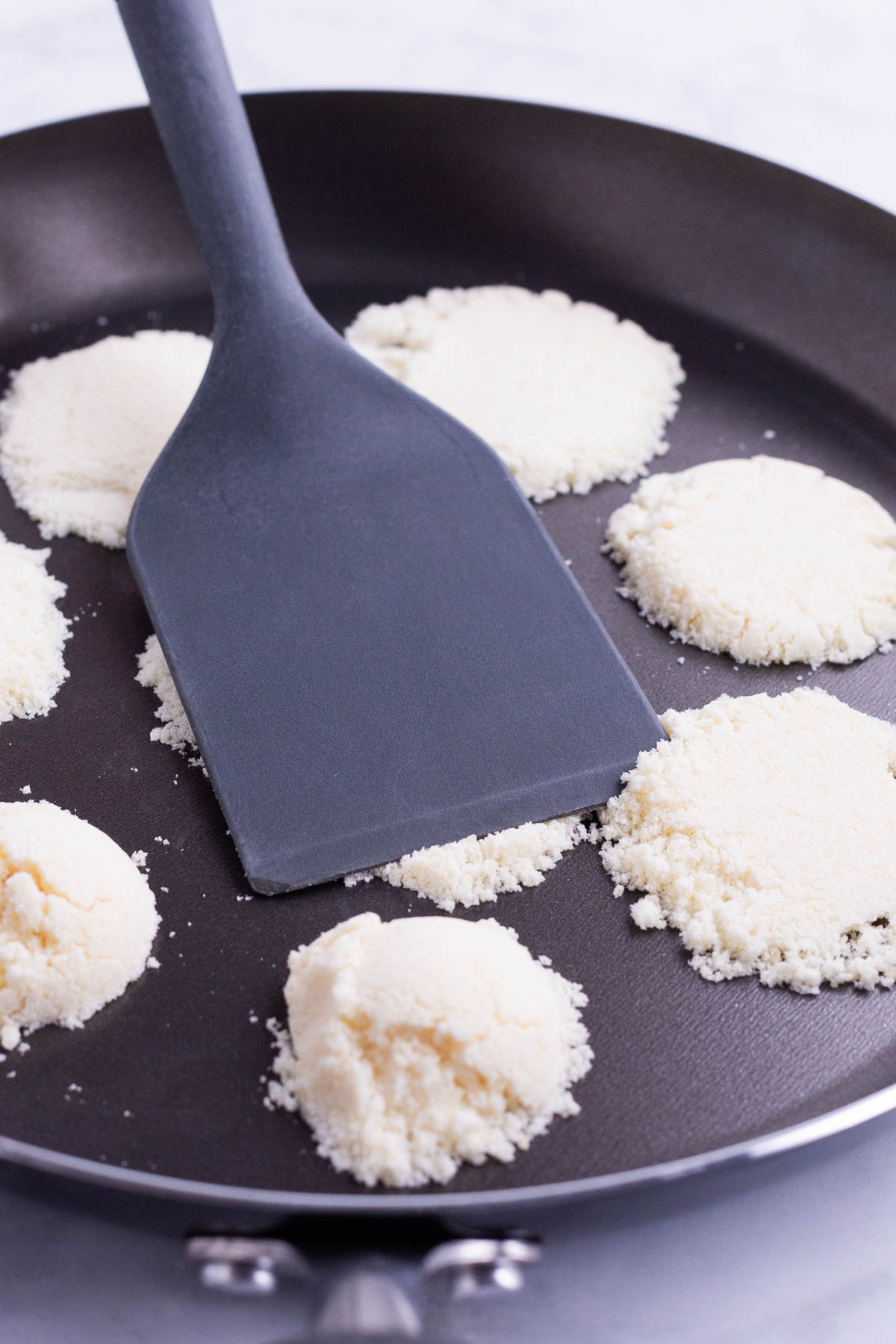 A spatula flattens Parmesan cheese in a skillet.