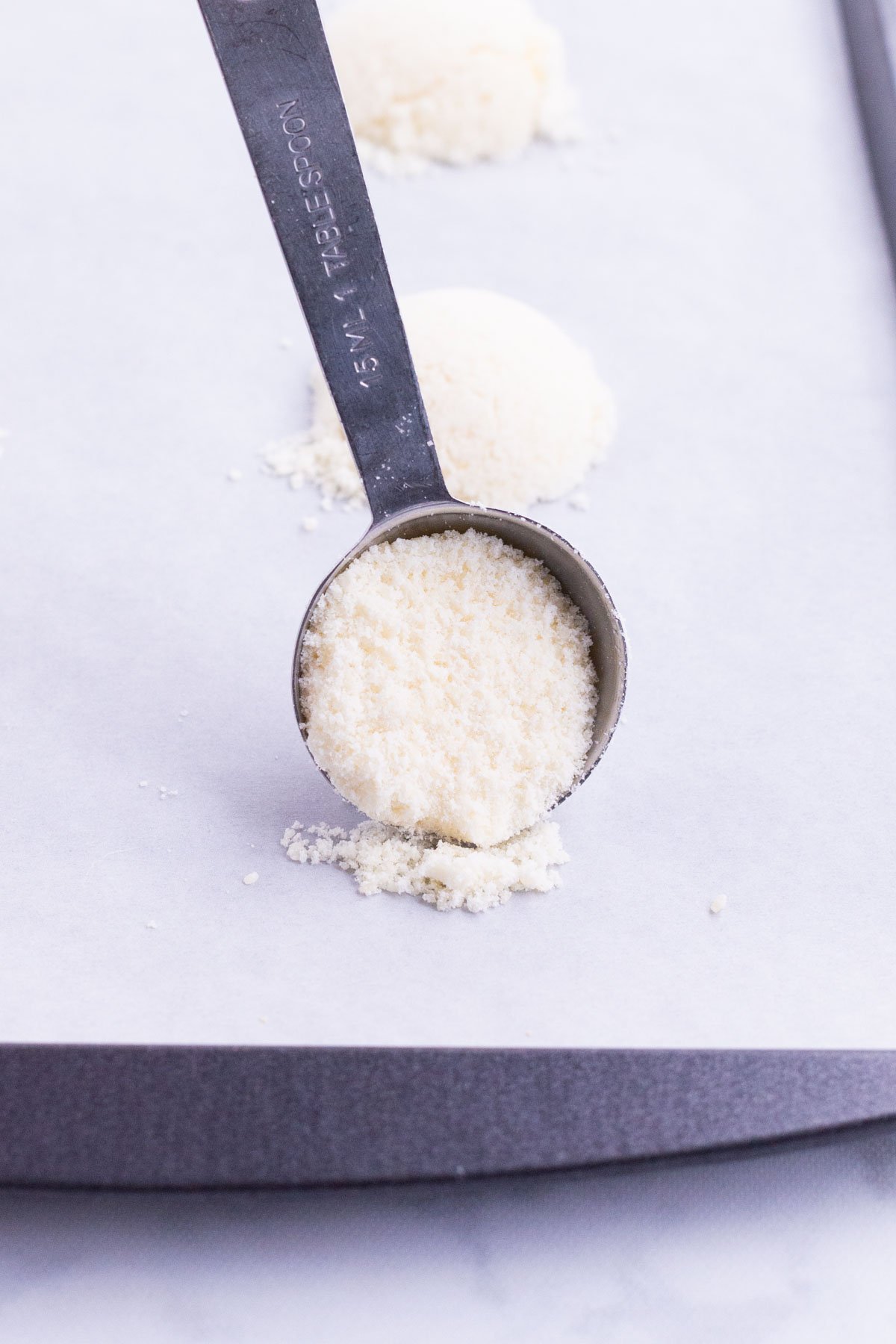 A spoon scoops Parmesan cheese onto a skillet.