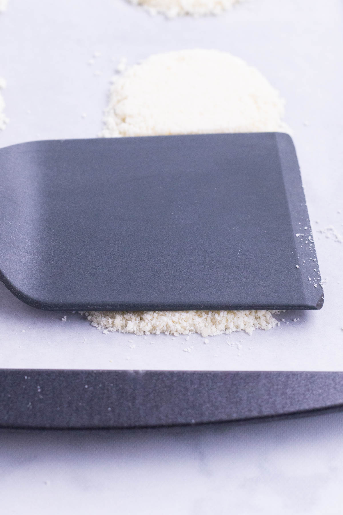 A spatula flattens Parmesan cheese in a baking tray.
