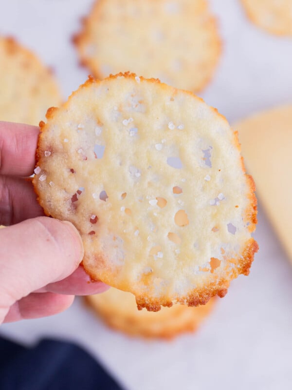 A hand holds a baked Parmesan crisp.