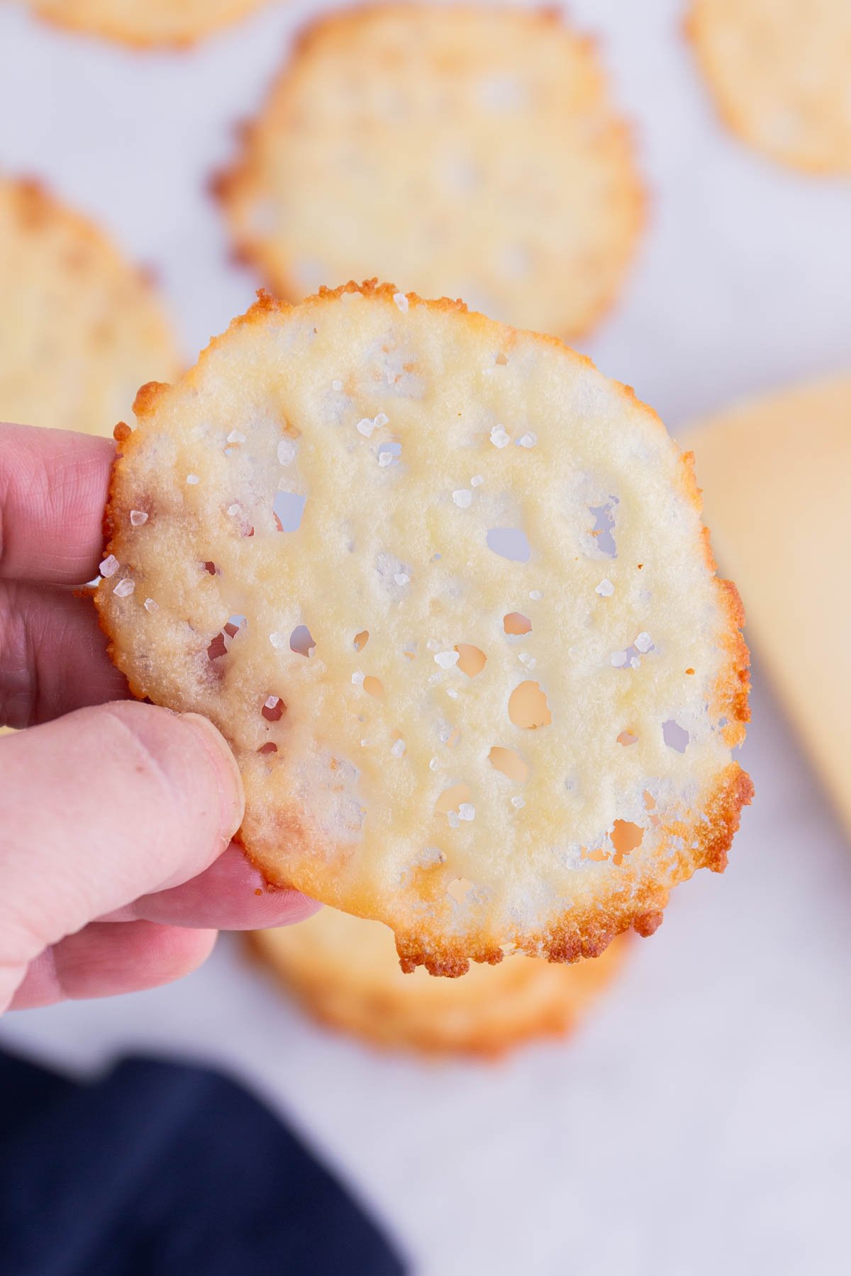 A hand holds a baked Parmesan crisp.