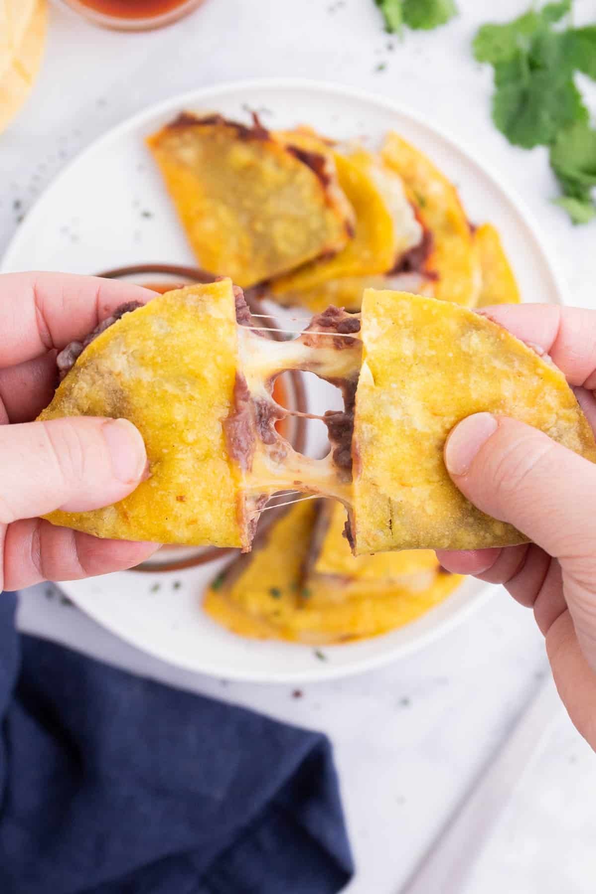 A hand rips a corn tortilla quesadilla in half.