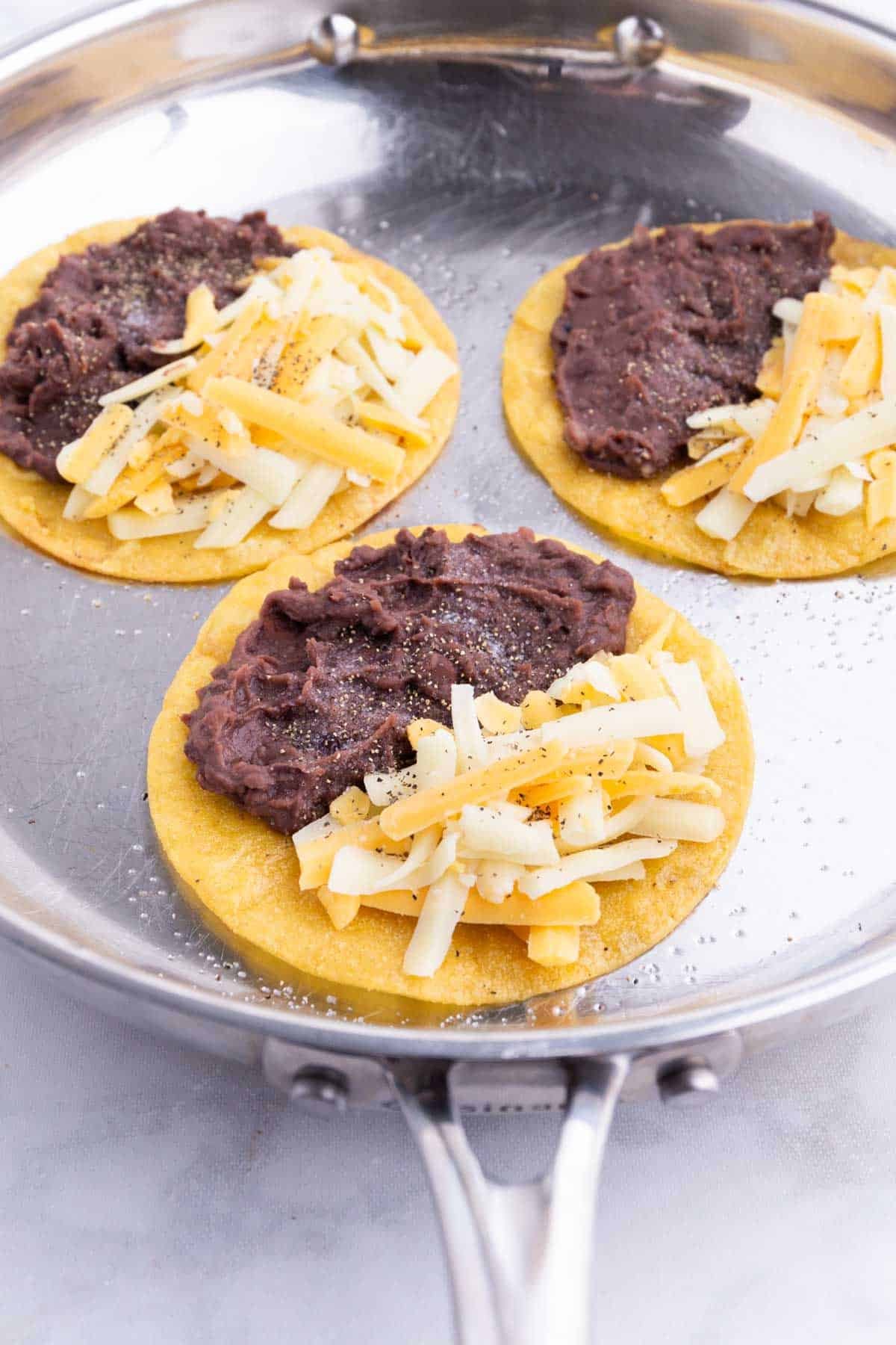 Cheese is added to the corn tortillas in a skillet.