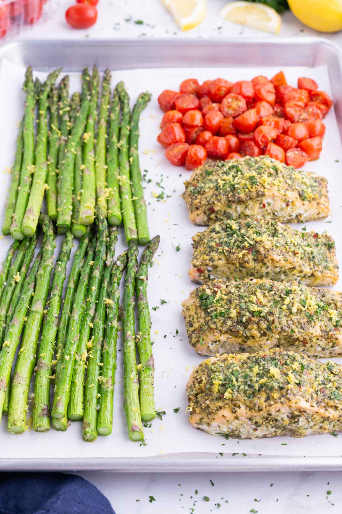 Asparagus, salmon, and tomatoes are baked on a tray in the oven.