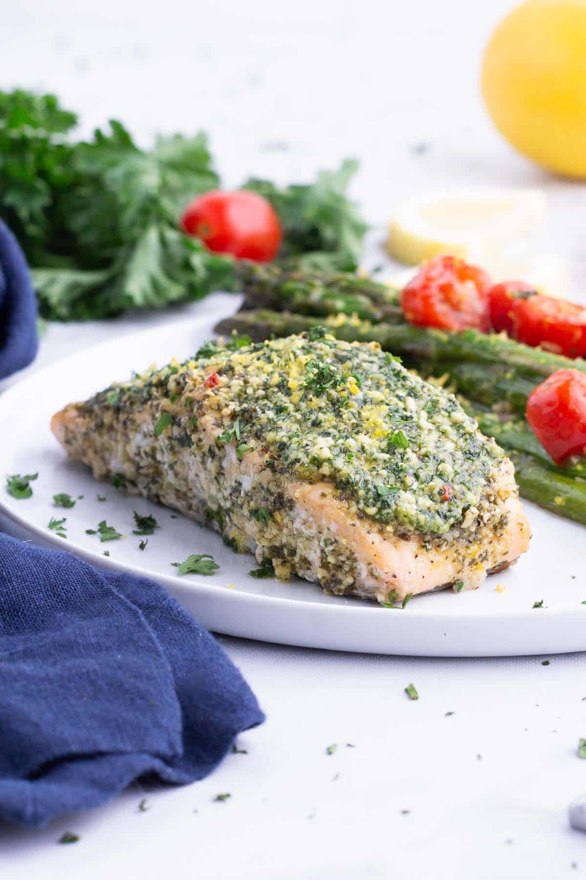 Pesto salmon is served on a plate with asparagus and tomatoes.