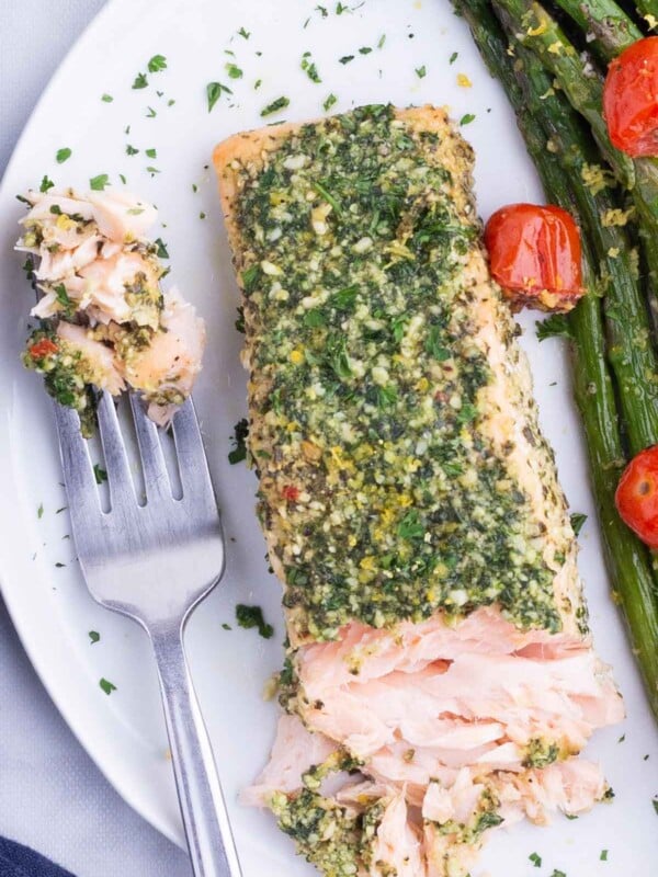 A fork digs into a fillet of pesto salmon and asparagus after cooking in the oven.