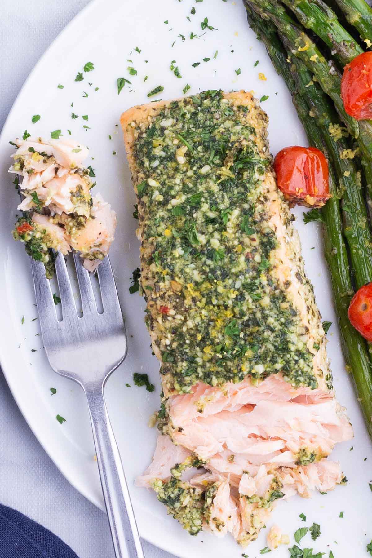 A fork digs into a fillet of pesto salmon and asparagus after cooking in the oven.