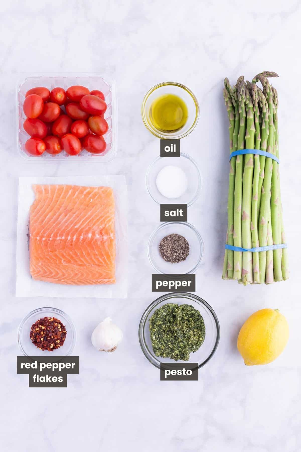 Salmon, asparagus, tomatoes, lemon, pesto, and seasonings are the main ingredients for this dish.